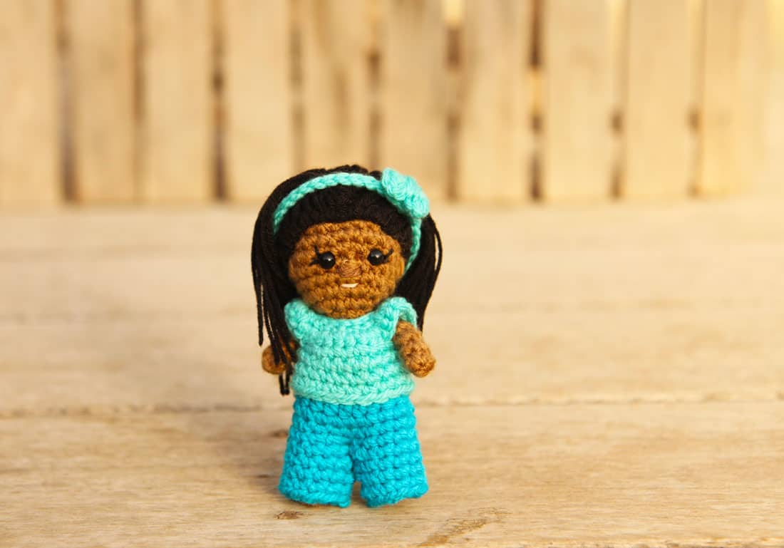small crochet doll with long hair, jeans, tshirt, and a hairband with a bow